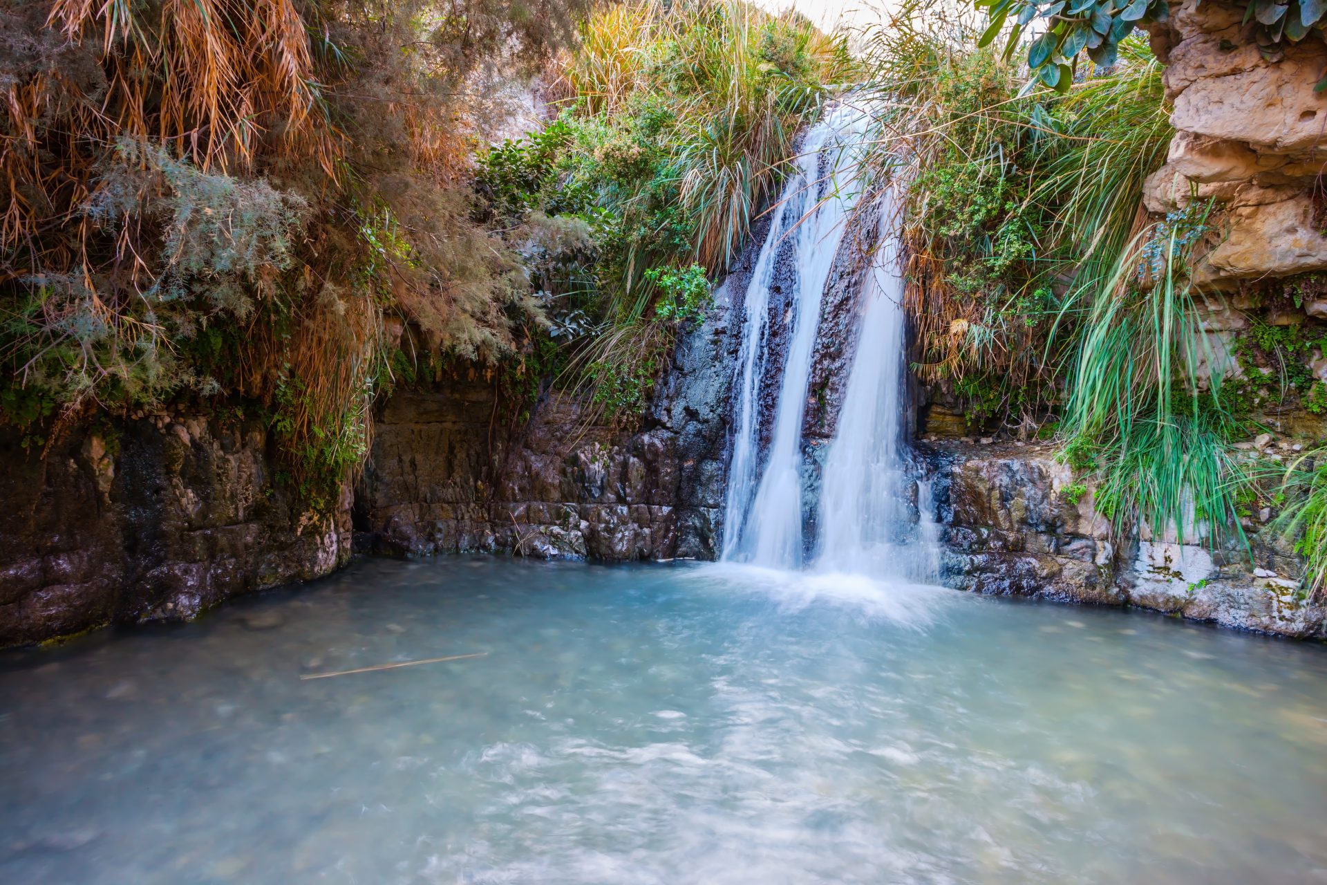Der malerische Wasserfall und ein kleiner tiefer See mit smaragdfarbenem Wasser. Wandern im Naturschutzgebiet Ein Gedi